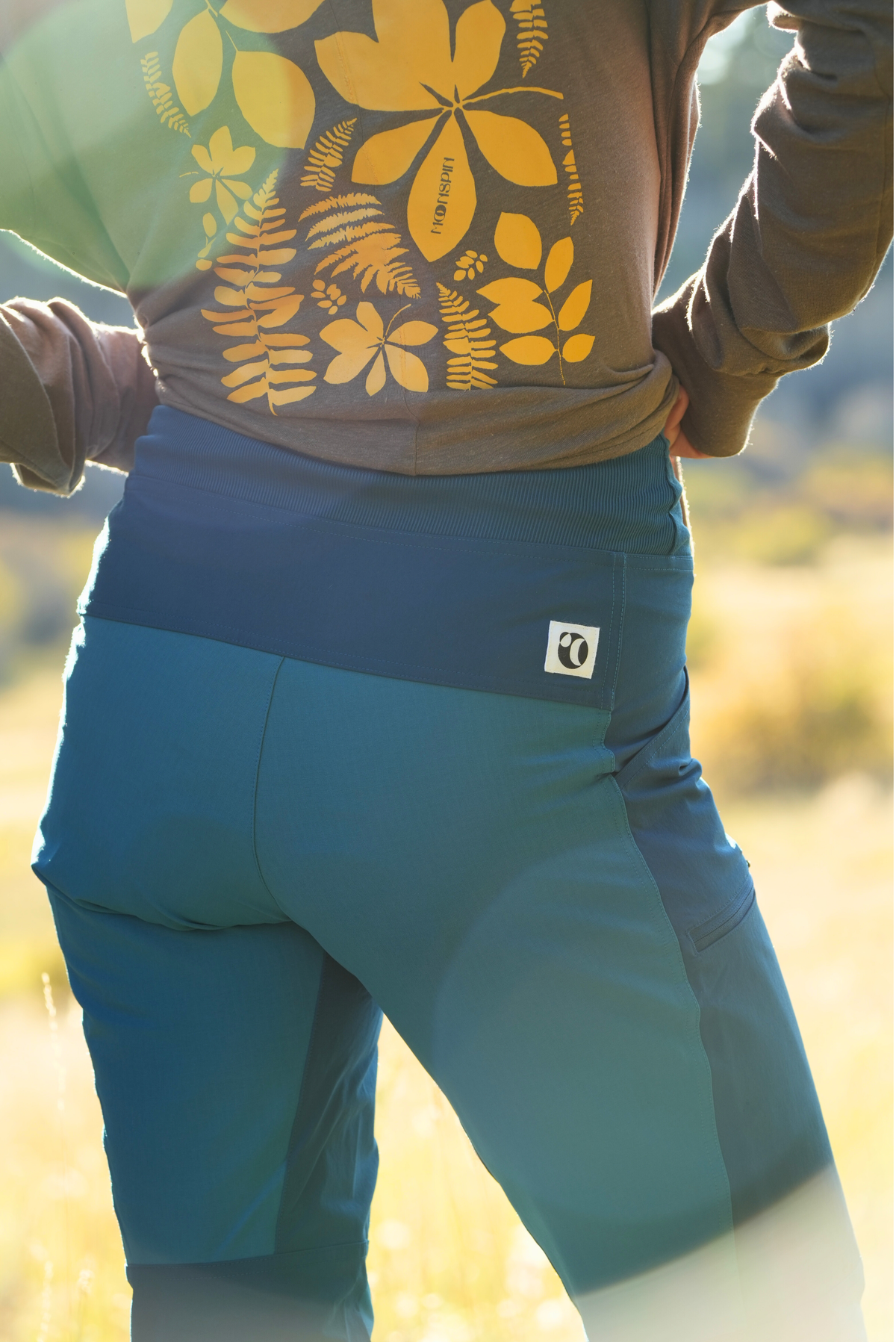 Woman wearing a brown top with yellow floral design and blue pants in a natural setting