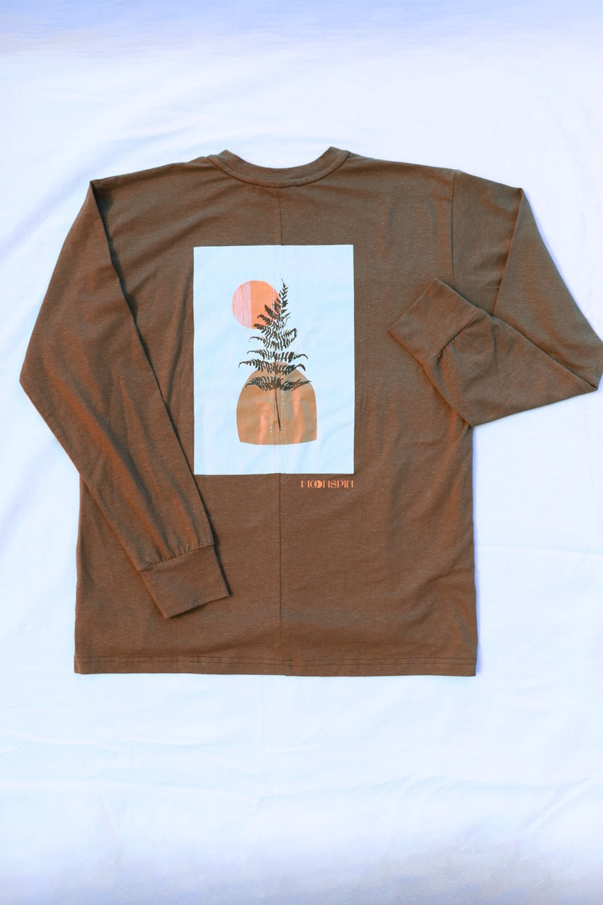 A brown long-sleeve t-shirt laid flat on a white fabric background, showing the back side with a large white graphic print of a fern and a moon, and small golden text below reading "Moonspin"
