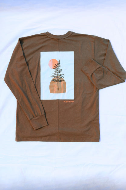 A brown long-sleeve t-shirt laid flat on a white fabric background, showing the back side with a large white graphic print of a fern and a moon, and small golden text below reading "Moonspin"